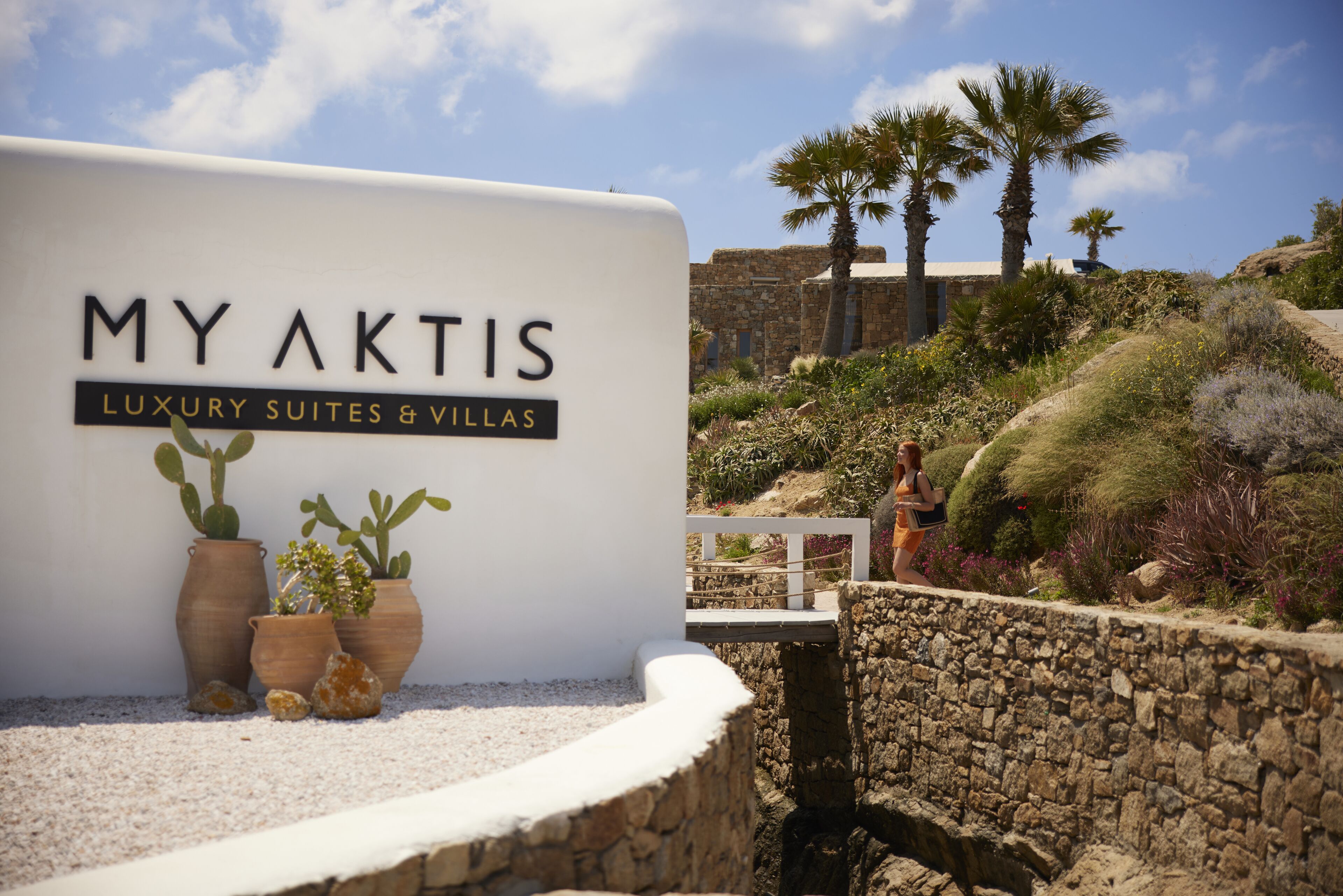 Senyal per a MyAktis Luxury Suites & Villas amb vista a palmeres i una paret de pedra.