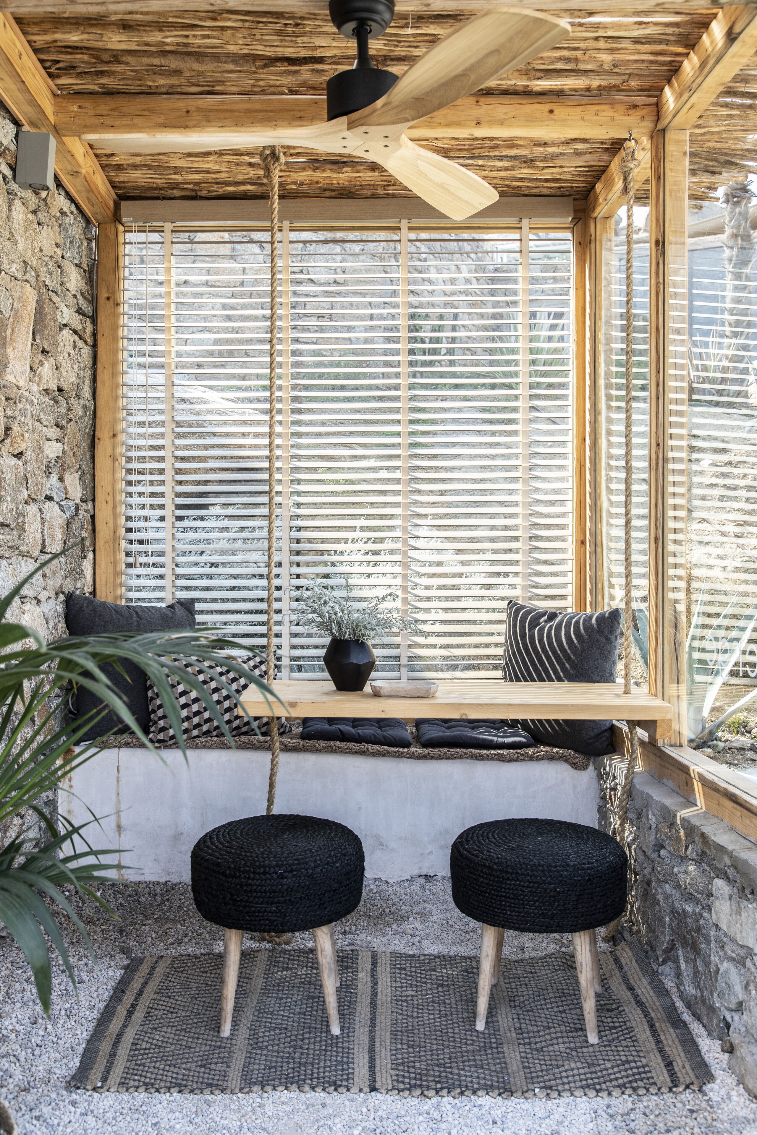A cozy seating area with a wooden bench, two black stools, and a potted plant.