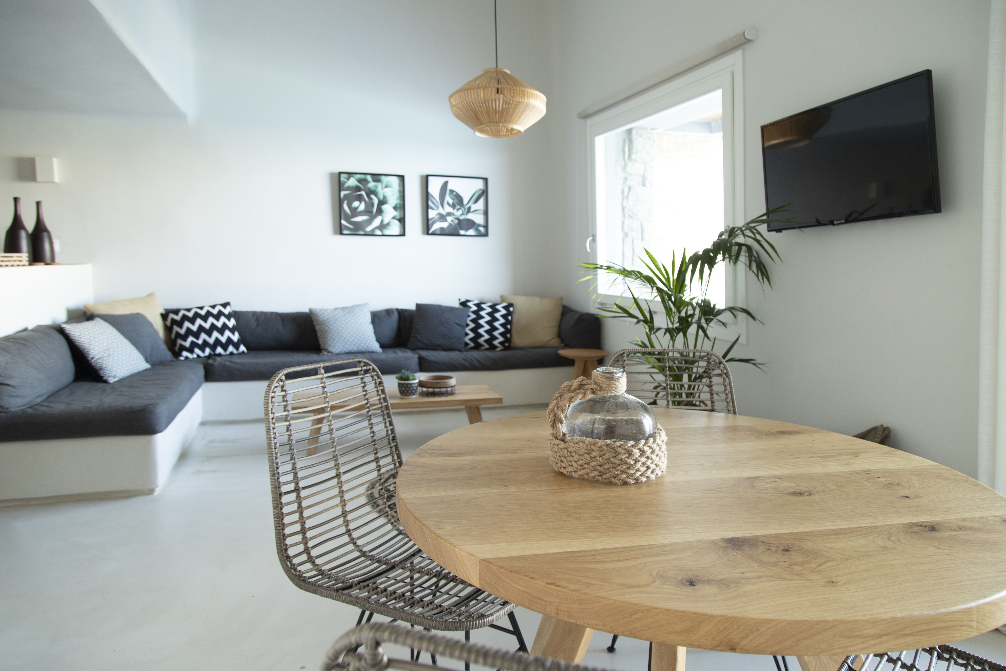 Ein modernes Wohnzimmer mit einem Holzespeisetisch, gewobenen Stühlen, einer Couch mit gemusterten Kissen und einem großen Fenster mit Blick.