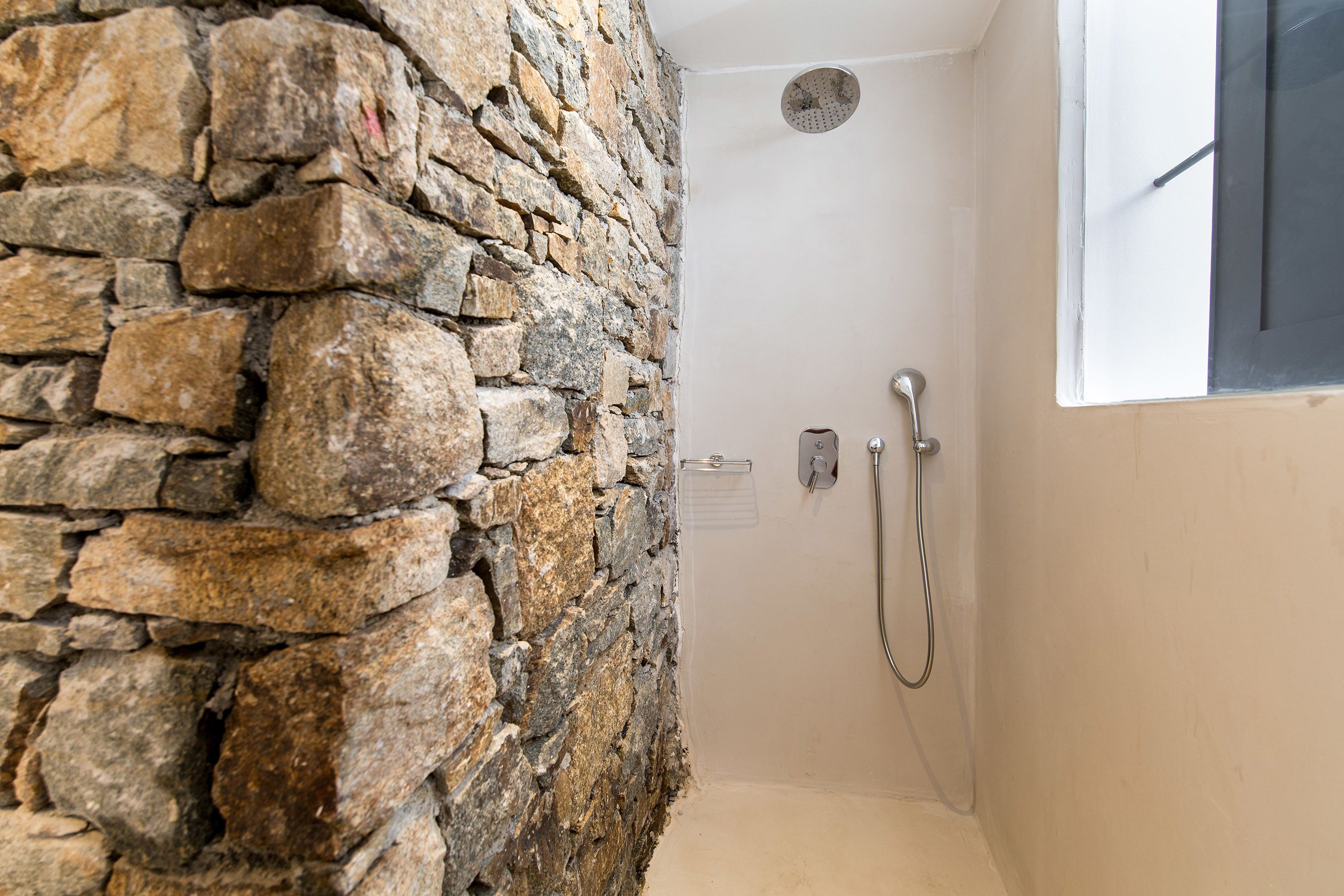 A shower area with a stone wall, a window, and a showerhead.