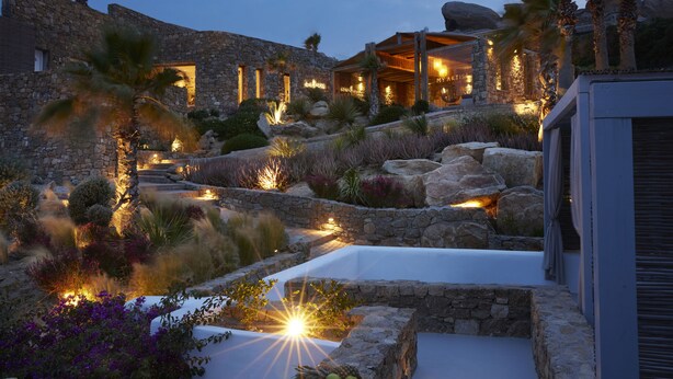 A stone building with a pool, surrounded by tropical plants and palm trees. - Nimbus My Aktis (Mykonos)