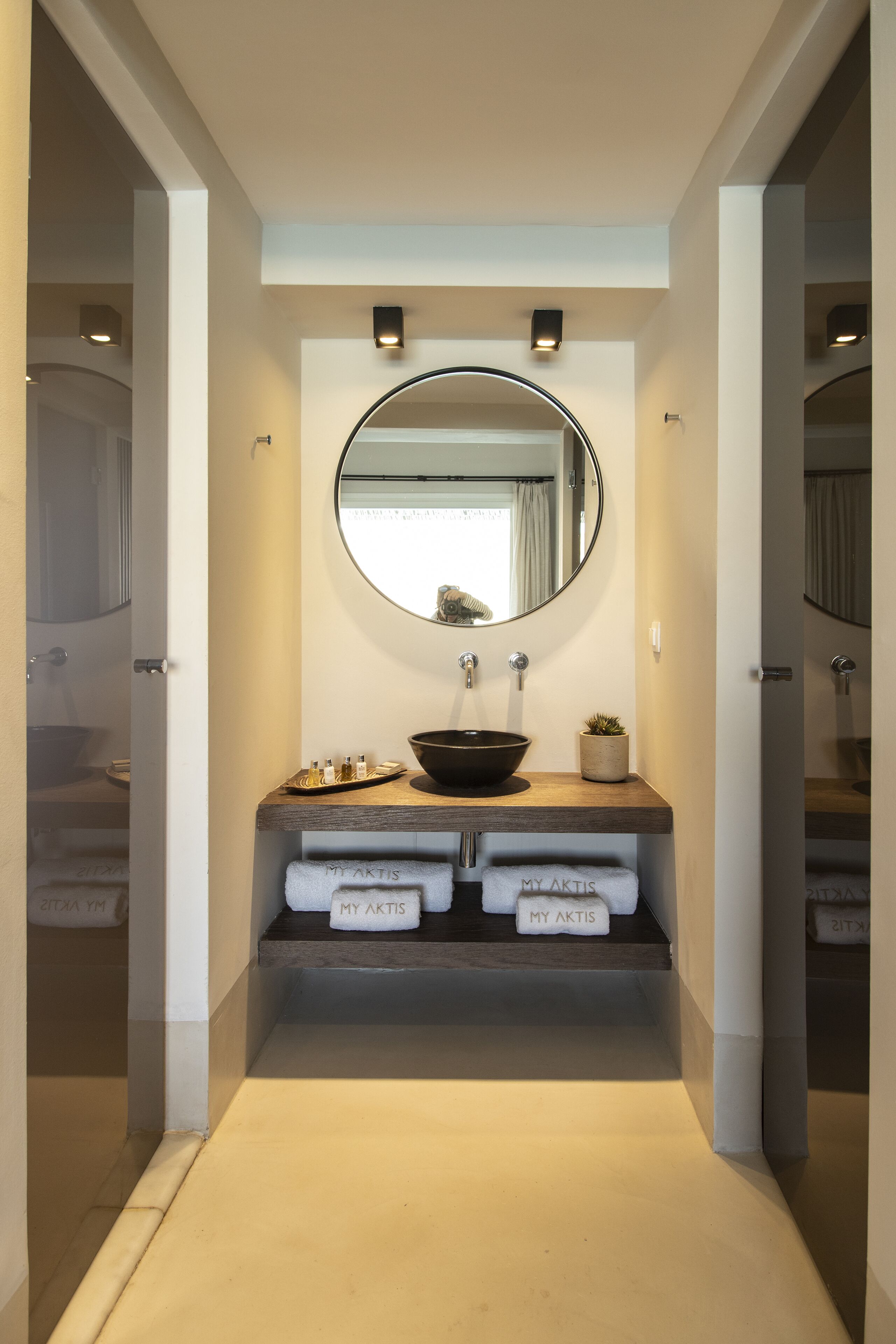 A modern bathroom with a round mirror, a sink, and two towel racks labeled "MY AKTIS".