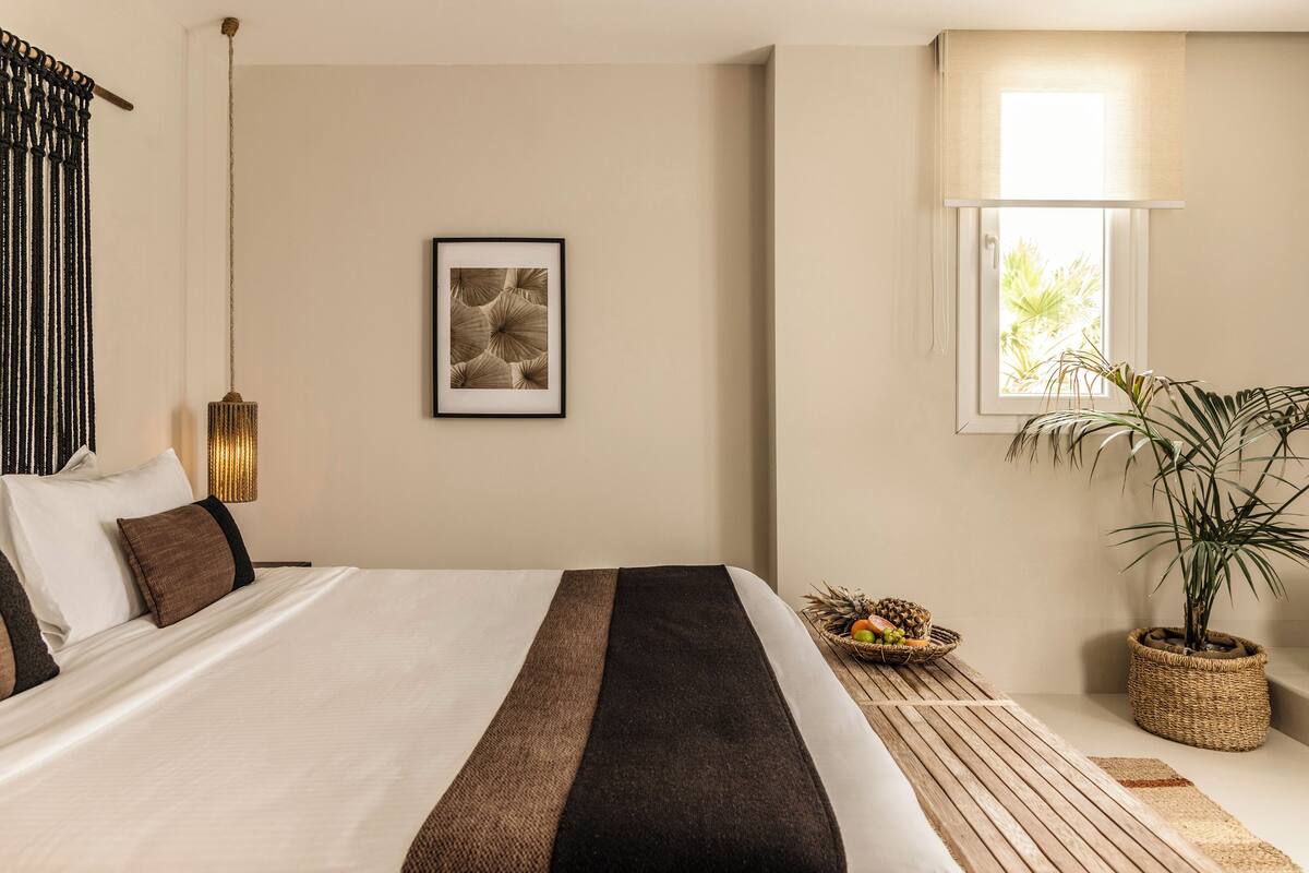 A neatly made bed with a striped bedspread, a framed artwork on the wall, and a window with a view of greenery.