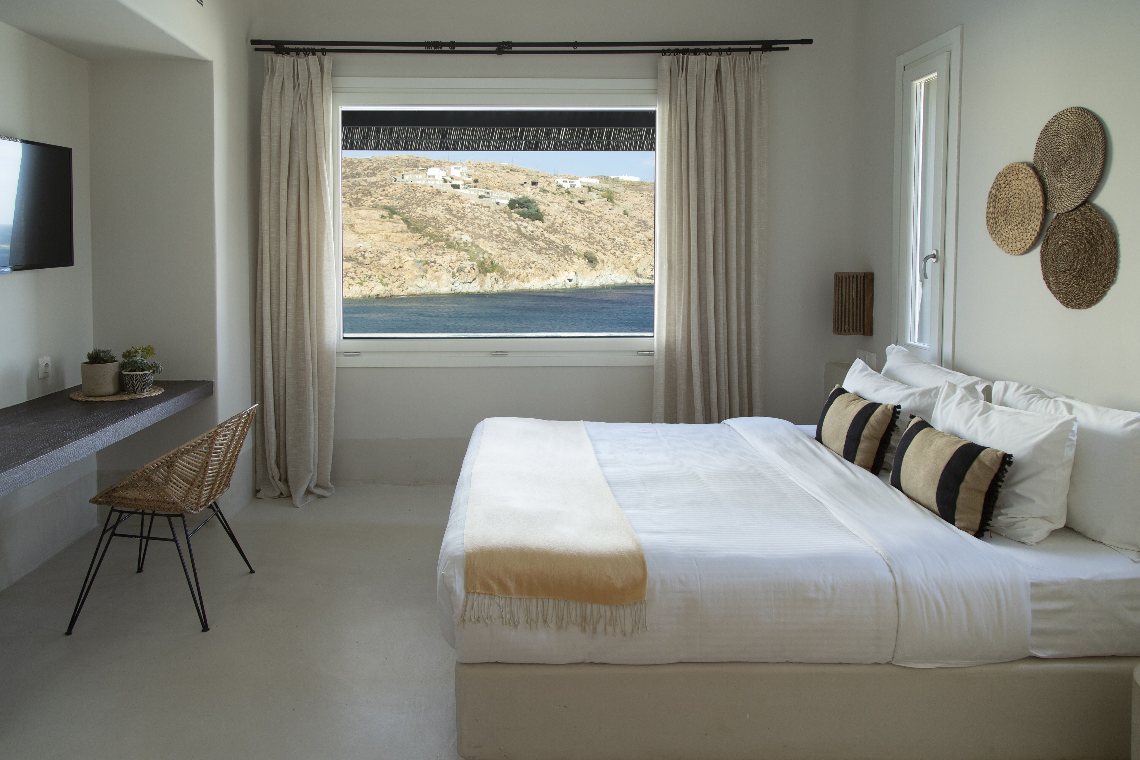 A bedroom with a bed, a desk, a chair, and a view of the sea.