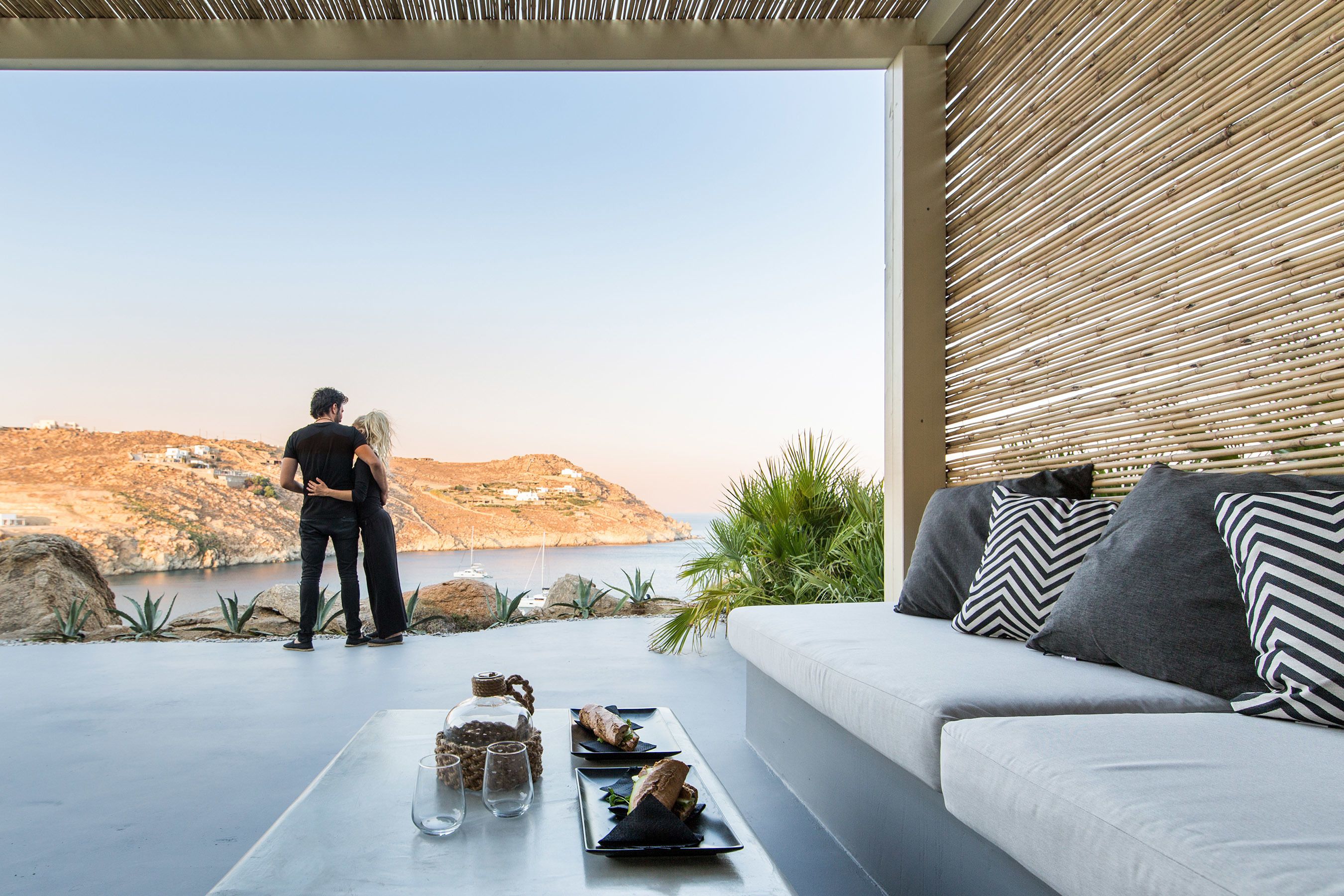 A modern outdoor seating area with a view of the sea and hills.