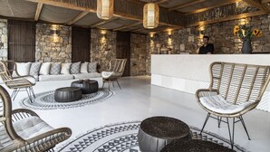 A spacious lounge area with a stone wall, wicker furniture, and a reception desk. - Nimbus My Aktis (Mykonos)