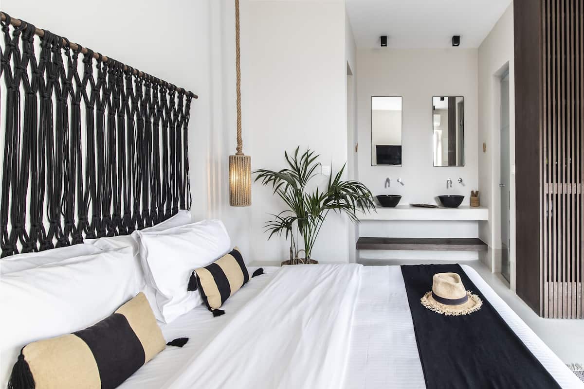 A modern bedroom with a bed, bedside plant, and a view of the bathroom.