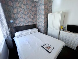 A neatly made bed with white linens, a bedside lamp, a wardrobe, a television, and a magazine on the bed.