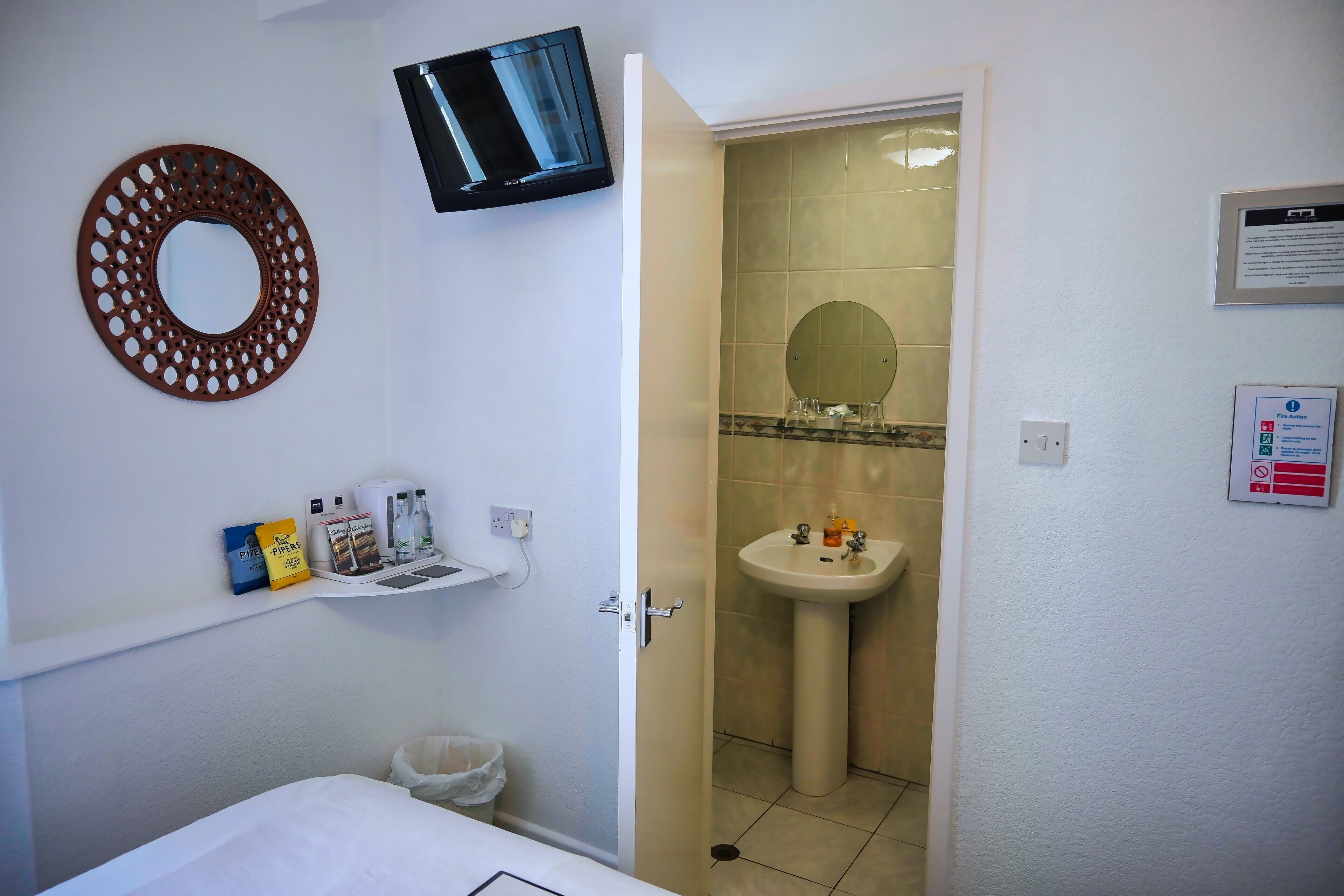 A hotel bathroom with a sink, mirror, and a television mounted on the wall.