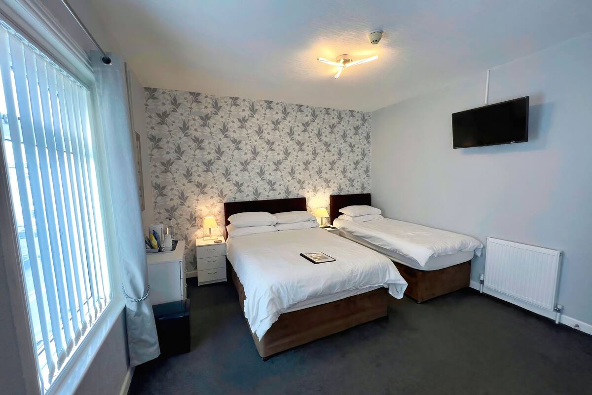 A hotel room with two beds, a TV on the wall, and a window with blinds.