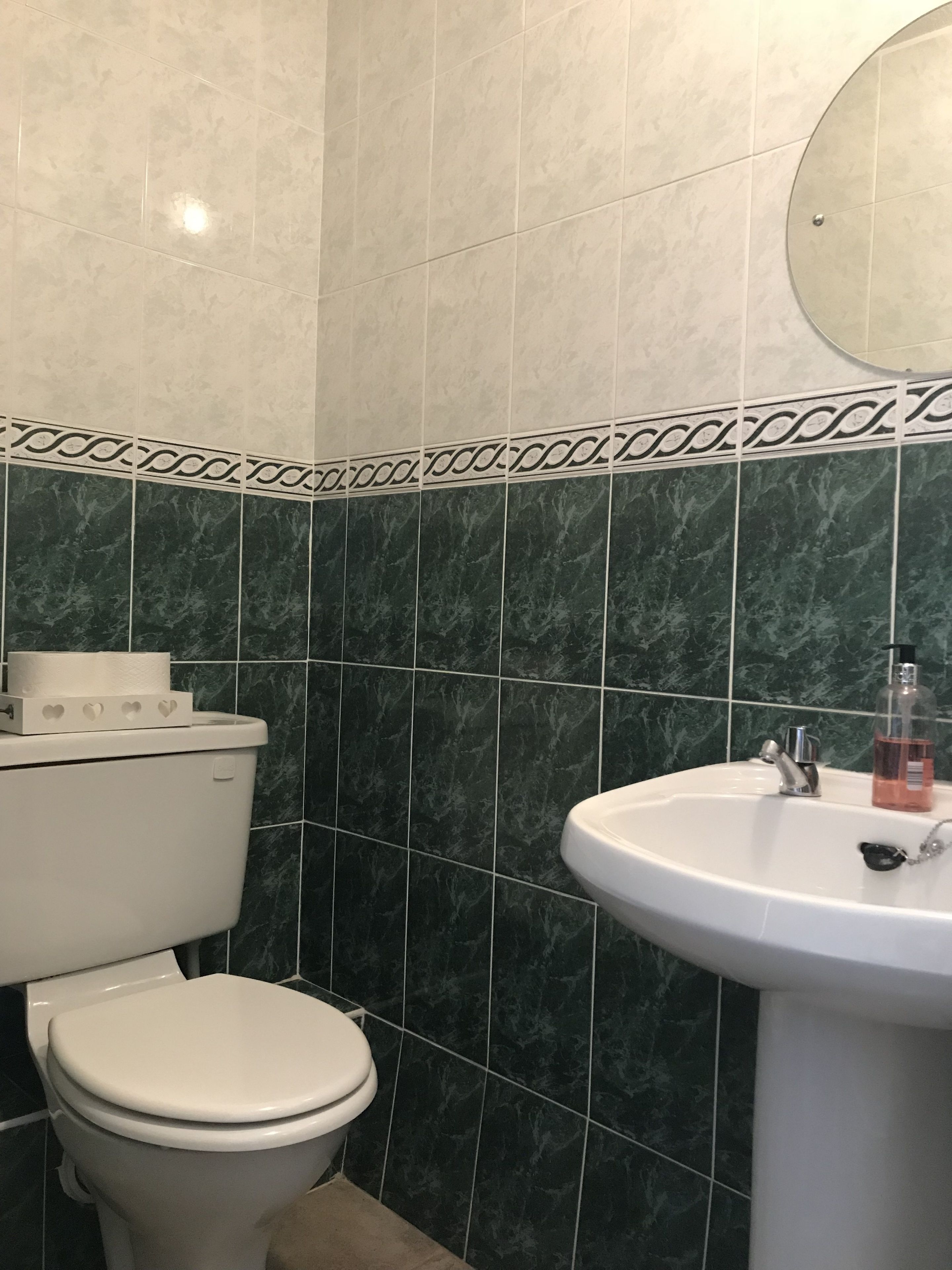 A bathroom with a toilet, sink, and green marble tiles.