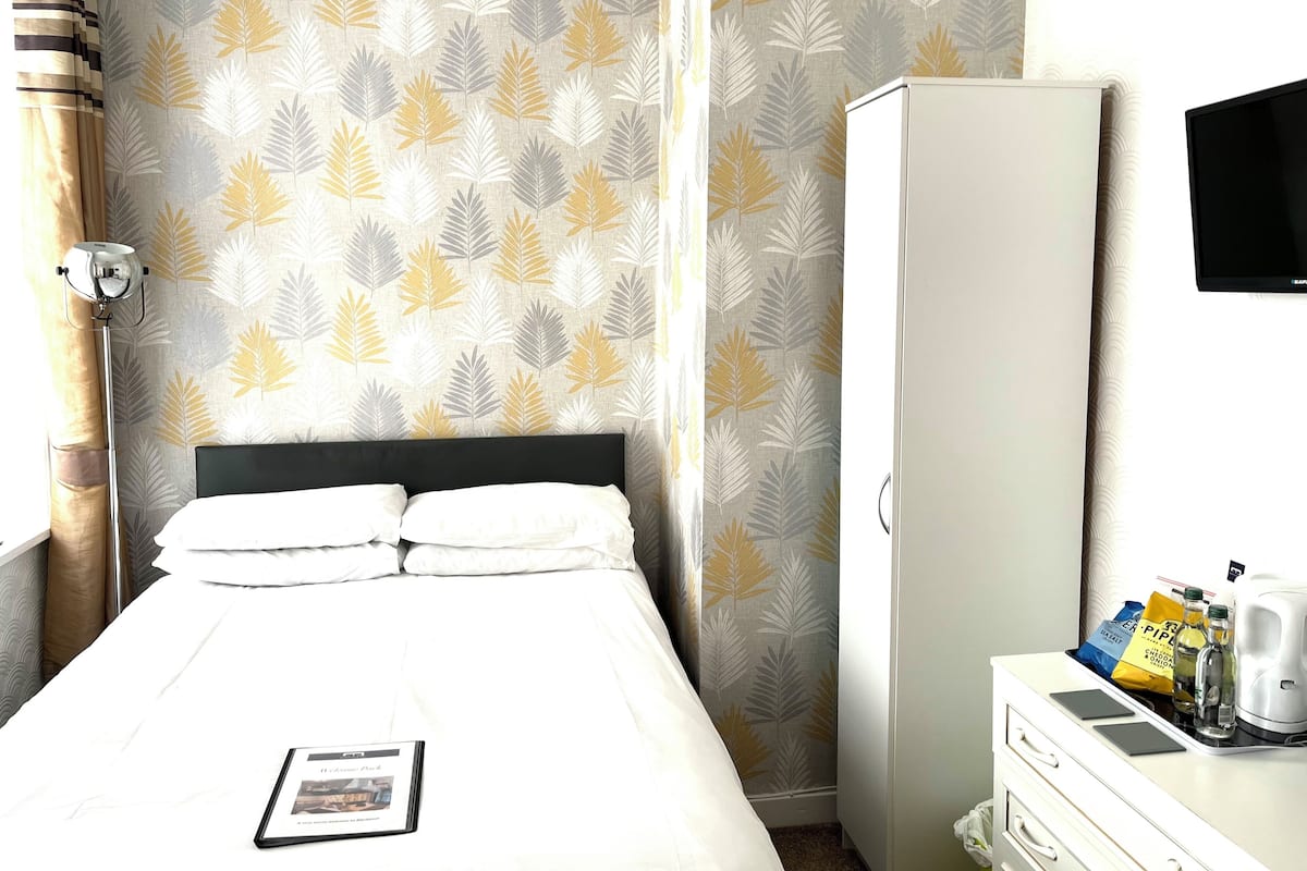 A hotel room with a bed, a wardrobe, a desk with a kettle, and a flat-screen TV.
