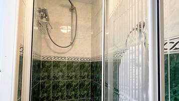Een douchecabine met een glazen deur, een handdouche en een bad.