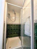 Een douchecabine met een glazen deur, een handdouche en een bad.