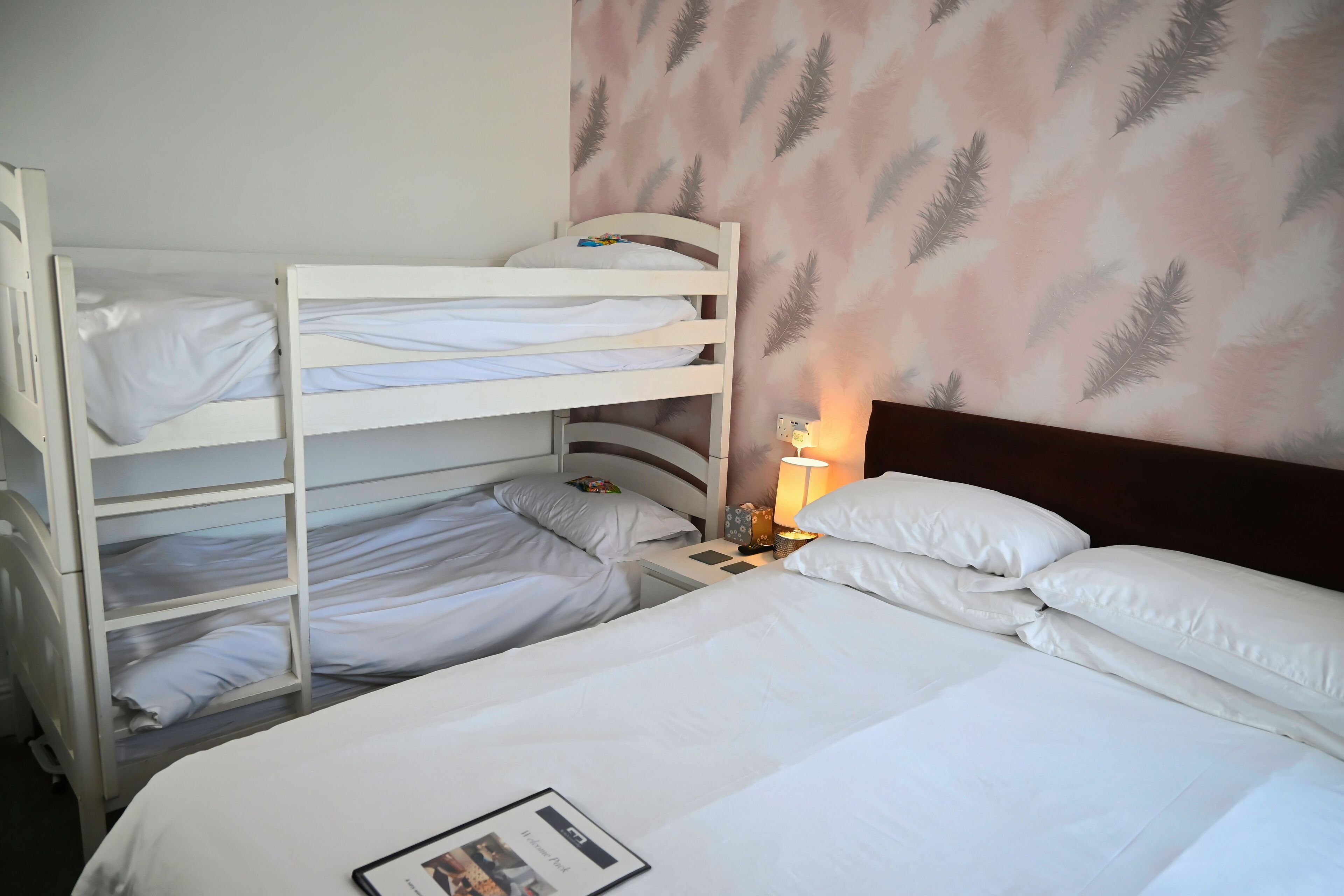 A hotel room with bunk beds, a bedside table with a lamp, and a feather-patterned wall.