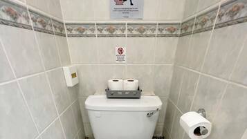 A small, tiled bathroom with a toilet, a paper towel holder, and a toilet paper roll.