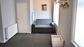 A compact room with a grey sofa, a white radiator, a door, a small wall-mounted shelf with clothes, and a basket. - Bella Vista Lodge (Blackpool)