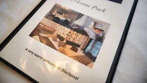 A welcome pack for a hotel room with a bed, a sofa, and a window. - Bella Vista Lodge (Blackpool)