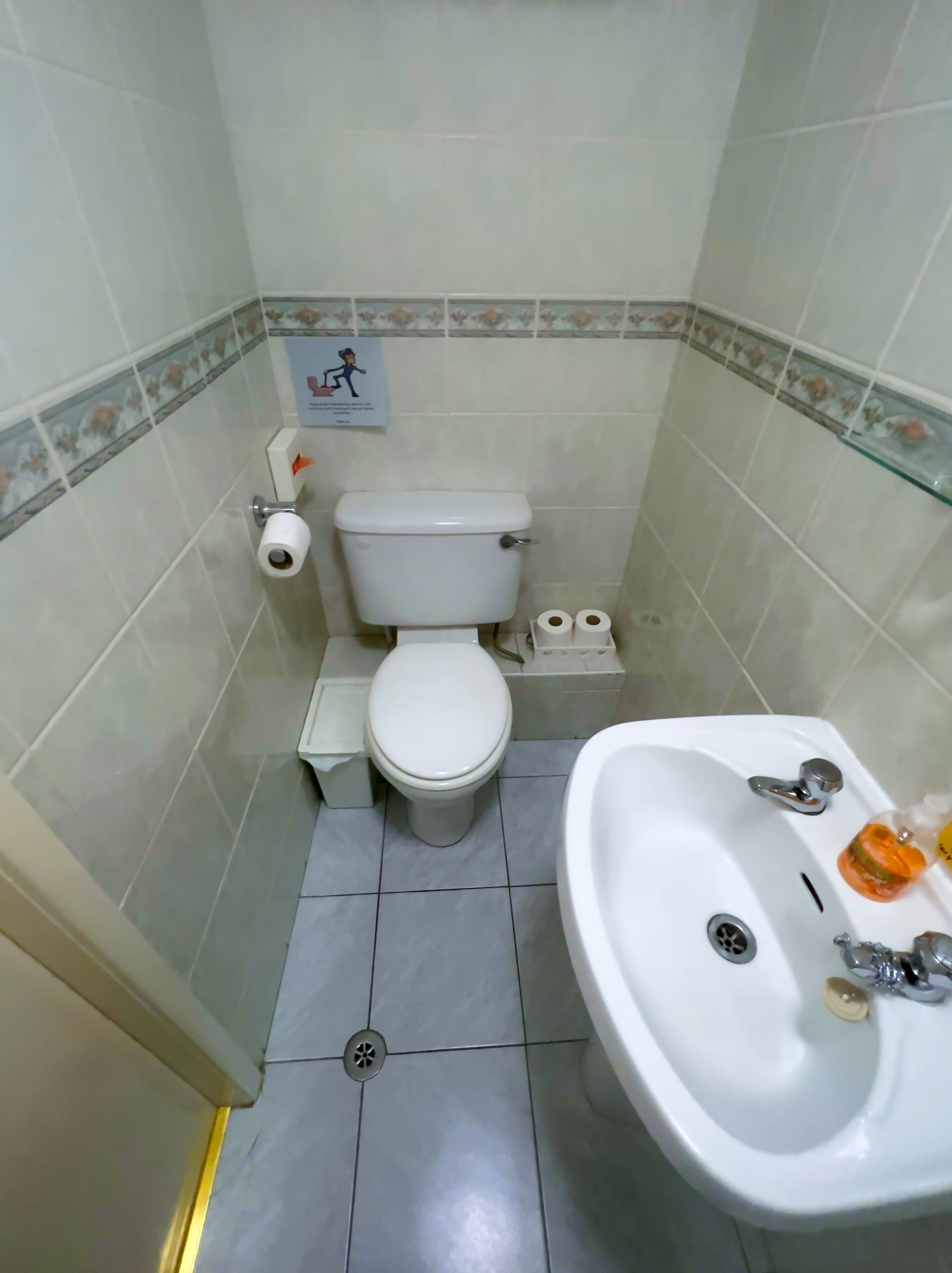 Un baño pequeño con inodoro, lavamanos y un cubo de basura.