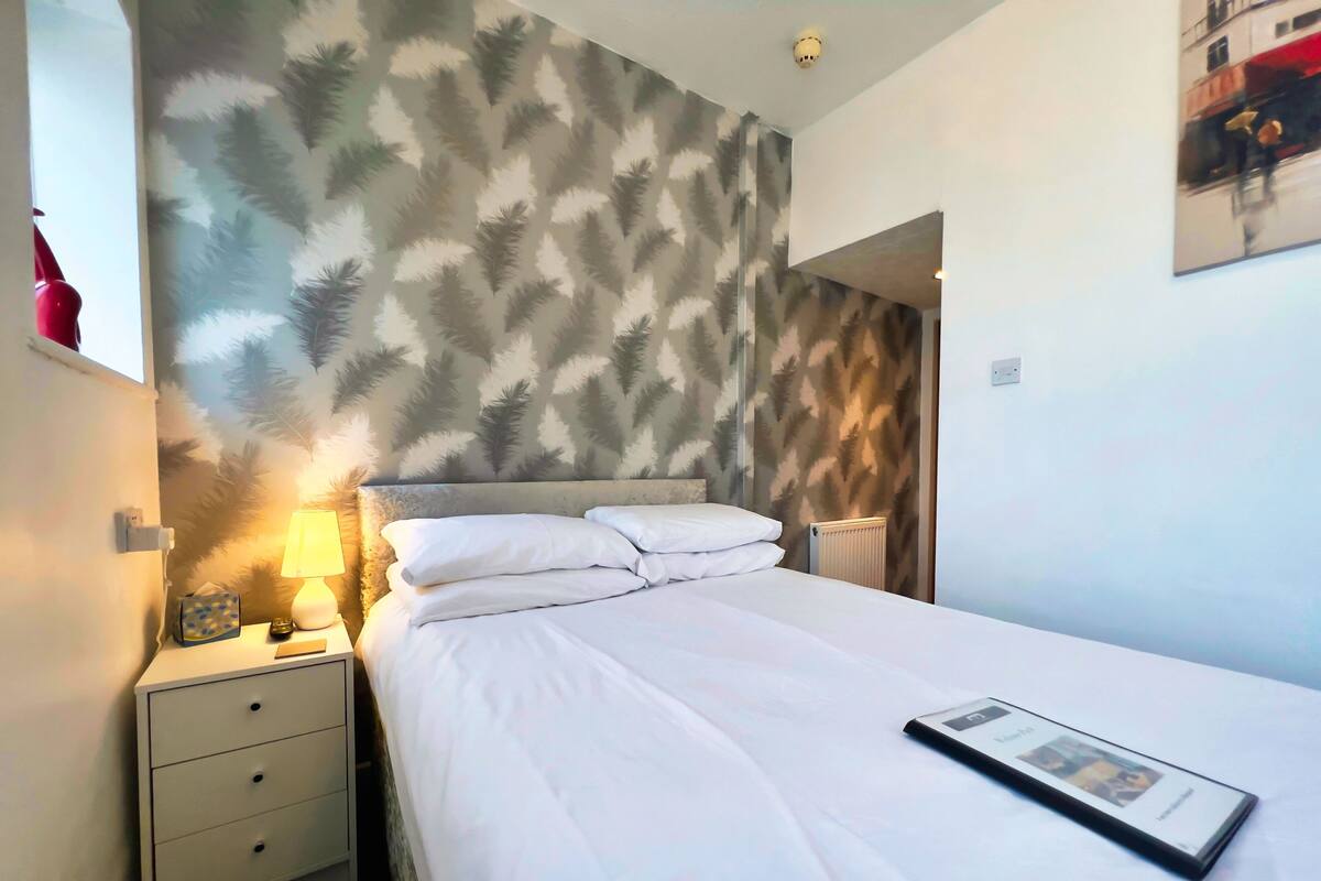 A hotel room with a bed, a nightstand, a lamp, and a wall with a leaf pattern.