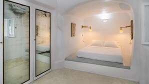 A bedroom with a bed, two wall-mounted lamps, and a small bench. - Cosmoia Cave House (Santorini)
