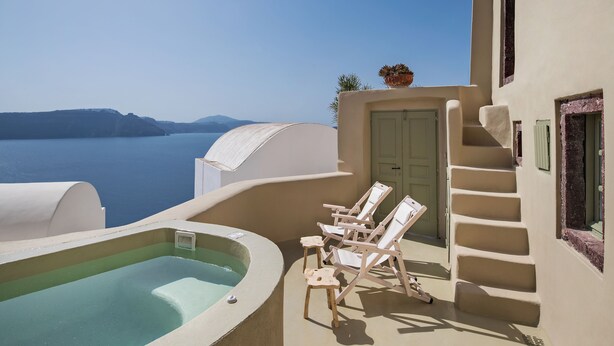 A balcony with a hot tub, lounge chairs, and a view of the sea. - Cosmoia Cave House (Santorini)