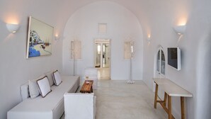 A modern, minimalist hotel room with a white sofa, a wooden coffee table, and a TV mounted on the wall. - Cosmoia Cave House (Santorini)
