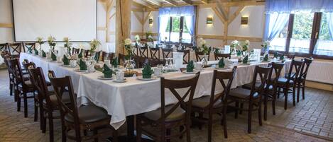 Una larga mesa de comedor dispuesta con sillas, manteles blancos y servilletas verdes.