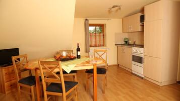 Una cocina compacta con armarios de madera, una mesa de comedor con sillas, un televisor y una ventana con cortinas.