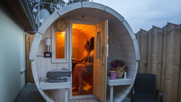 Una sauna de madera con un reloj, toallas y una planta en maceta.