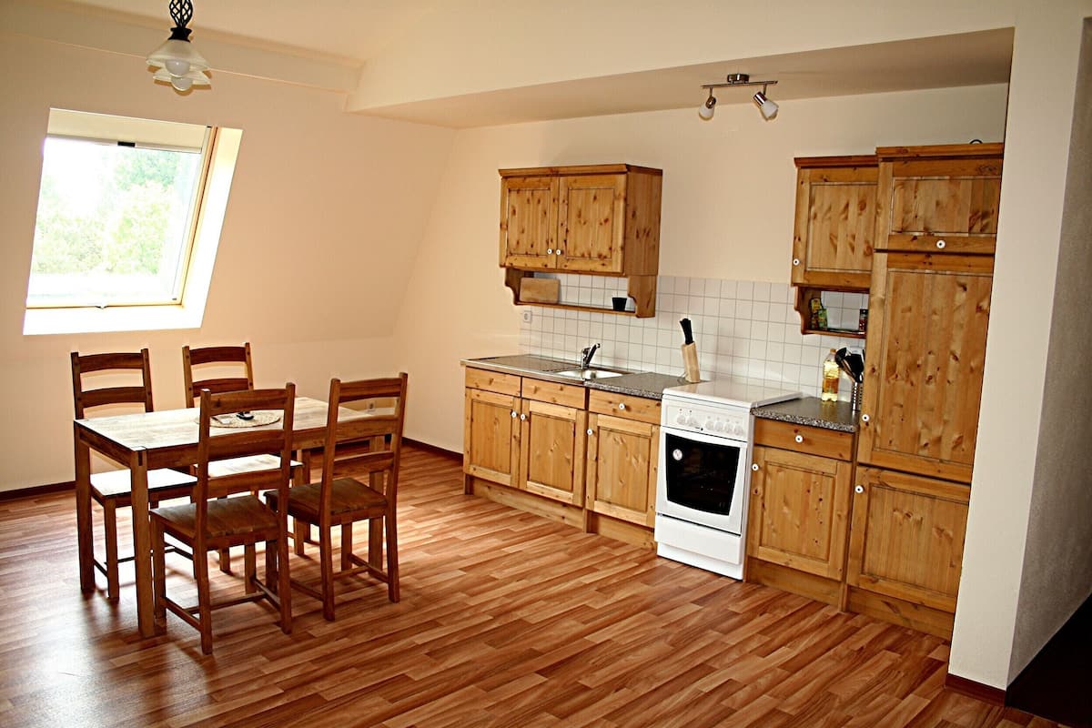 Une cuisine avec des meubles de rangement en bois, une cuisinière et une table à manger avec des chaises.