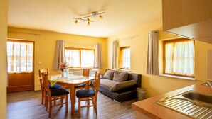 Una sala de estar luminosa con una mesa de comedor, sillas, un sofá y una cocina con un fregadero.