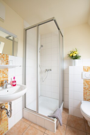 A shower with a glass door, a sink with a mirror, and a toilet. - Landgasthof Fischer (Freiberg)