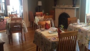 A dining room with wooden chairs and tables, a chandelier, a clock, and a fireplace. - Inn at Park Spring (Portland)