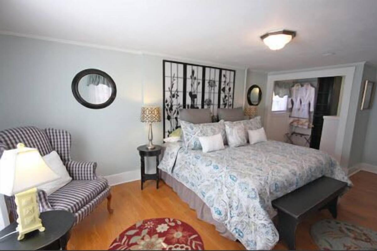 A bedroom with a bed, a chair, a lamp, and a mirror.