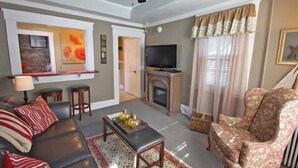 A living room with a sofa, armchairs, a coffee table, a fireplace, a television, and a ceiling fan. - Inn at Park Spring (Portland)