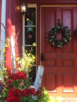 Una puerta roja con el número 135, un adorno floral y una ventana con los rótulos de Yelp y TripAdvisor.