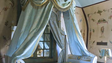 A four-poster canopy bed with a bench, a small table, and a lamp.