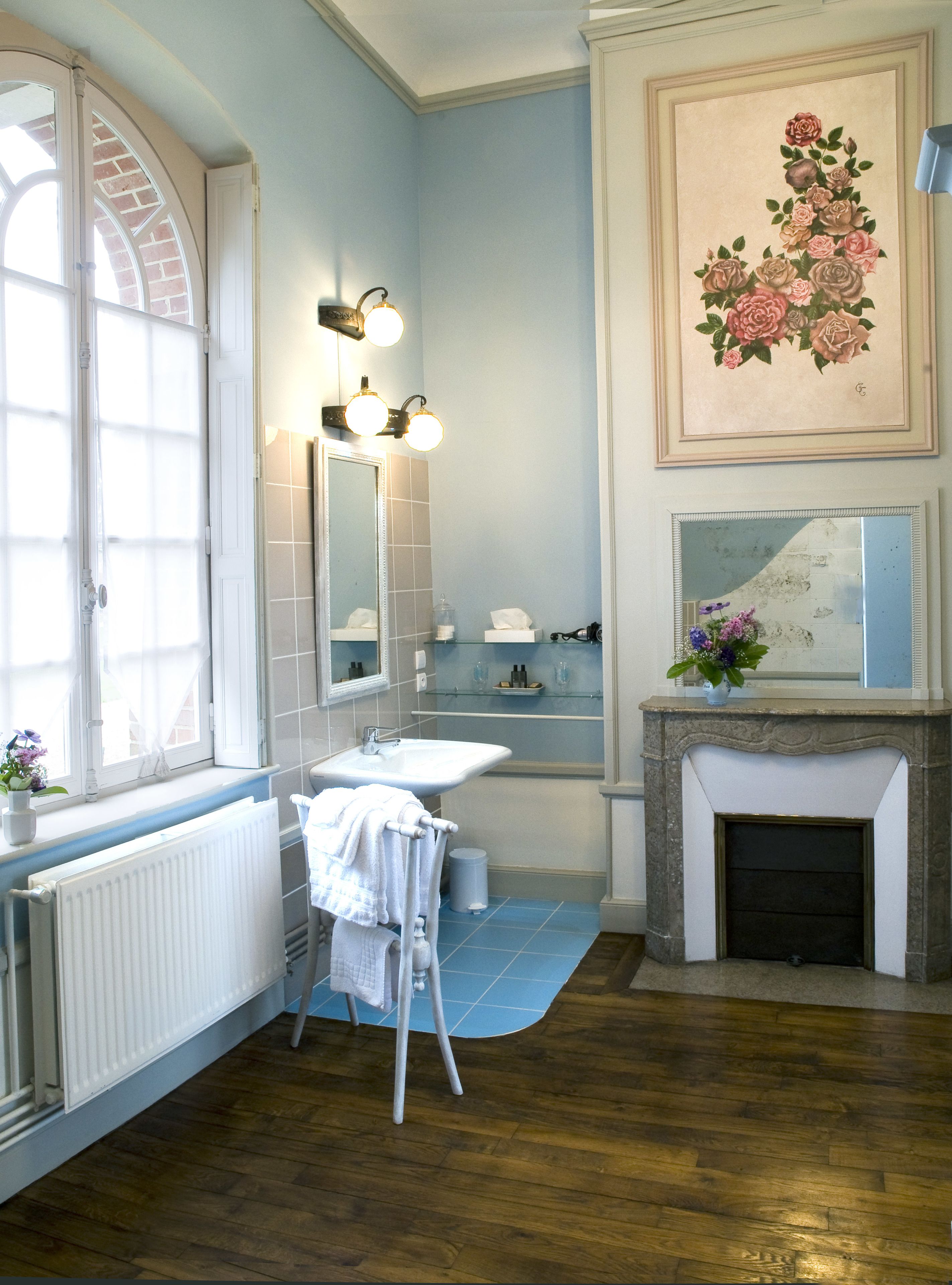 Une salle de bain avec une grande fenêtre, un lavabo, un miroir, une cheminée et un tapis bleu.