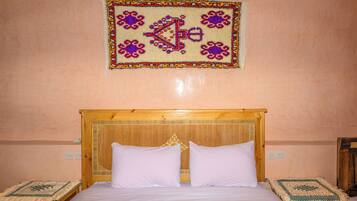 A bedroom with a wooden bed, two pillows, a decorative wall hanging, and two bedside tables with patterned tablecloths.