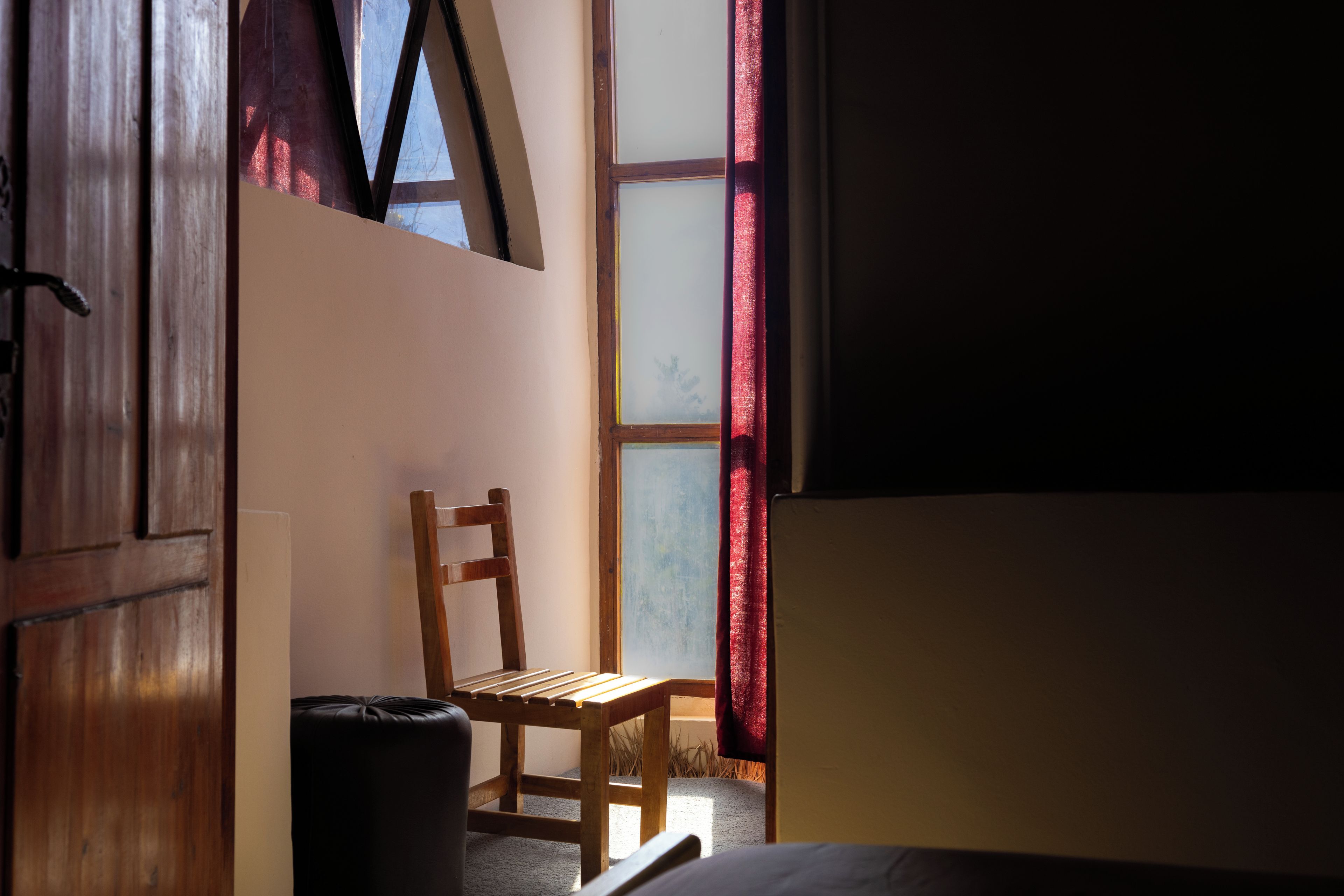 A room with a wooden chair, a trash bin, and a window with red curtains.