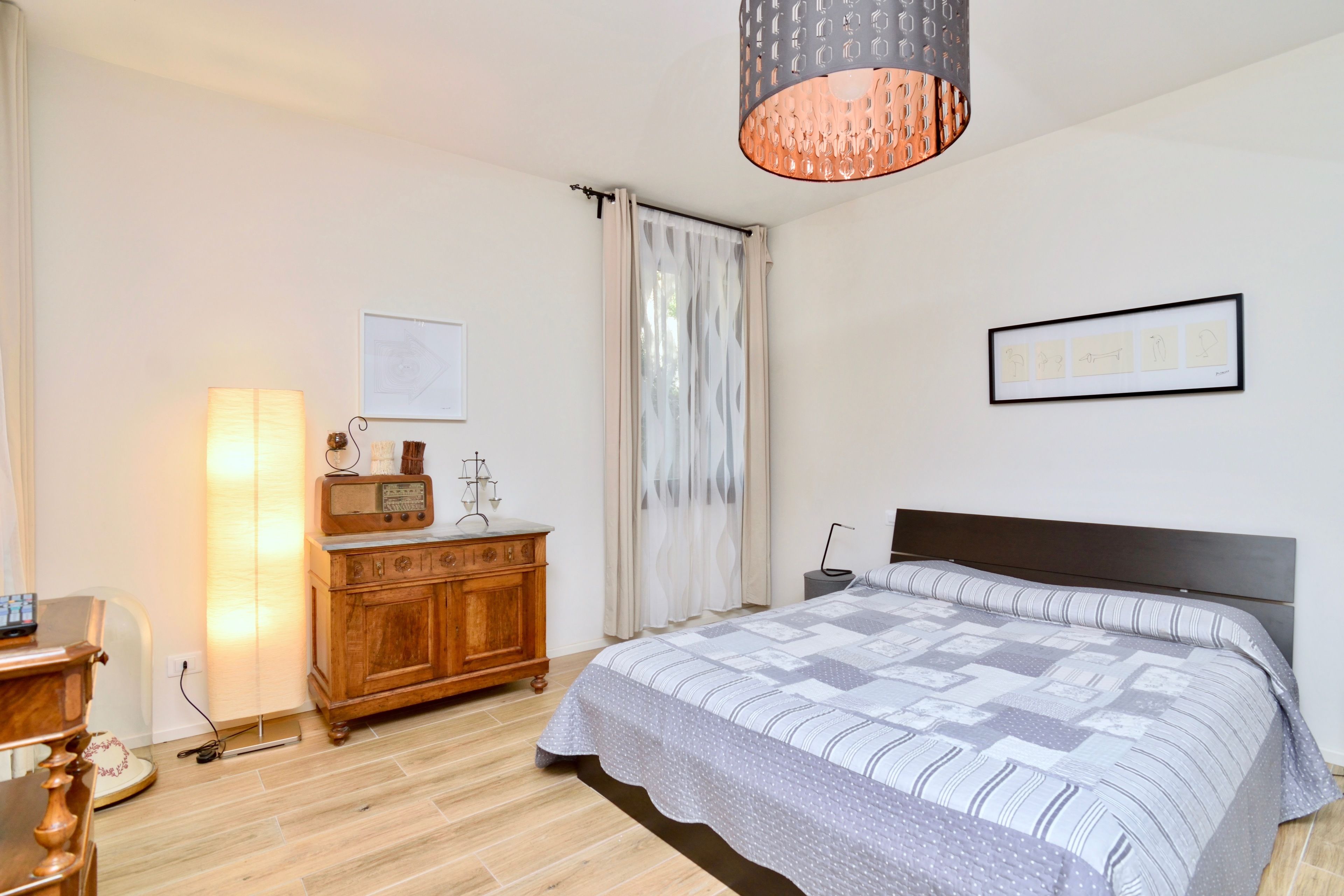 A bedroom with a bed, wooden dresser, radio, and a framed picture on the wall.