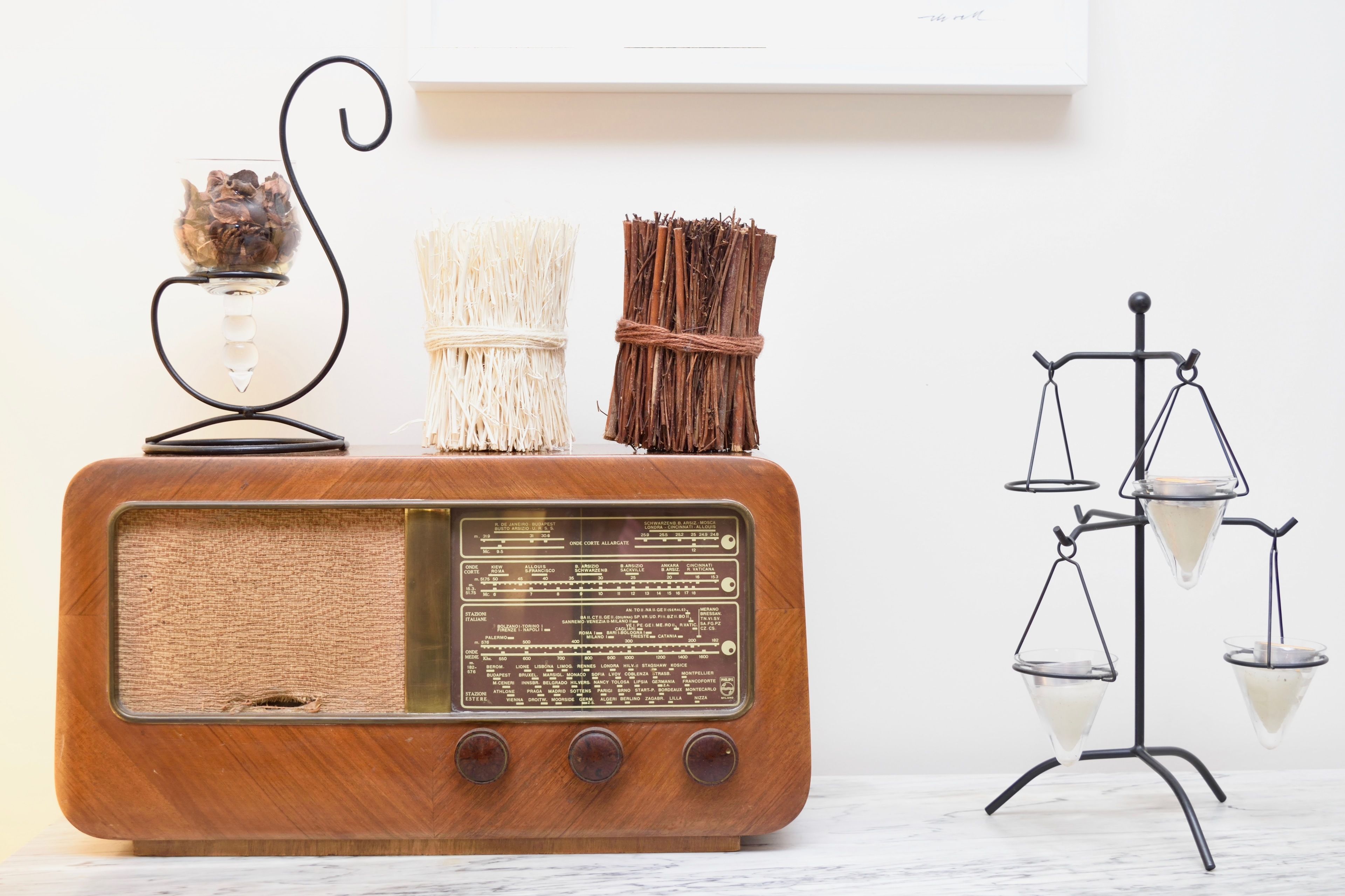 Une vieille radio en bois dotée d’un bouton de réglage, un vase contenant des fleurs séchées et une balance avec des récipients en verre.