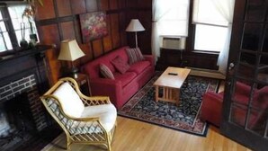 Ein gemütliches Wohnzimmer mit einem roten Sofa, einem Korbstuhl, einem kleinen Holztisch und einem Kamin.