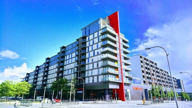 En modern byggnad med flera våningar, med ett framträdande rött, vertikalt element, stora fönster och en väl synlig butiksfasad med skyltar.
