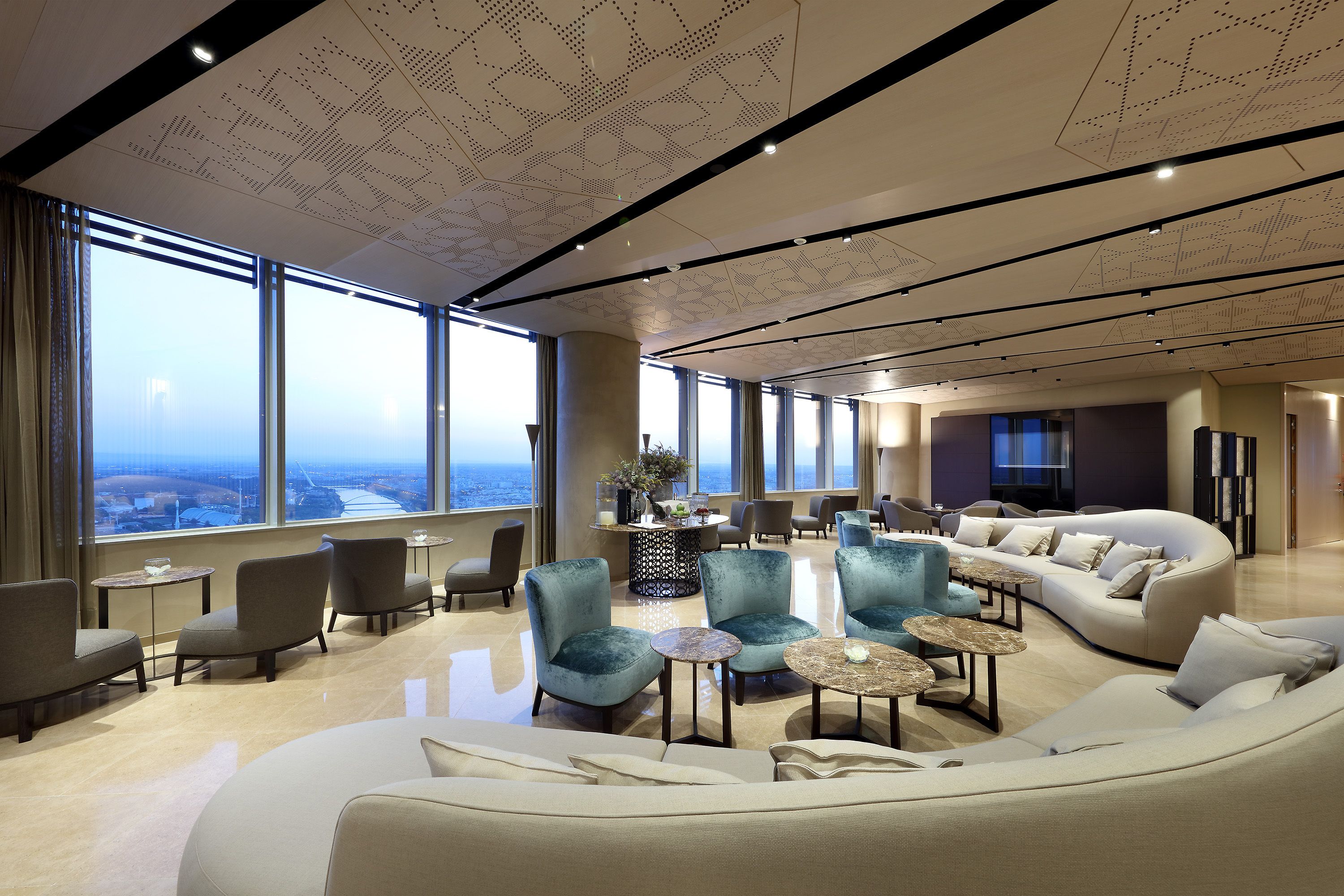 A spacious lounge area with a large window offering a city view, comfortable seating, and a modern ceiling design.