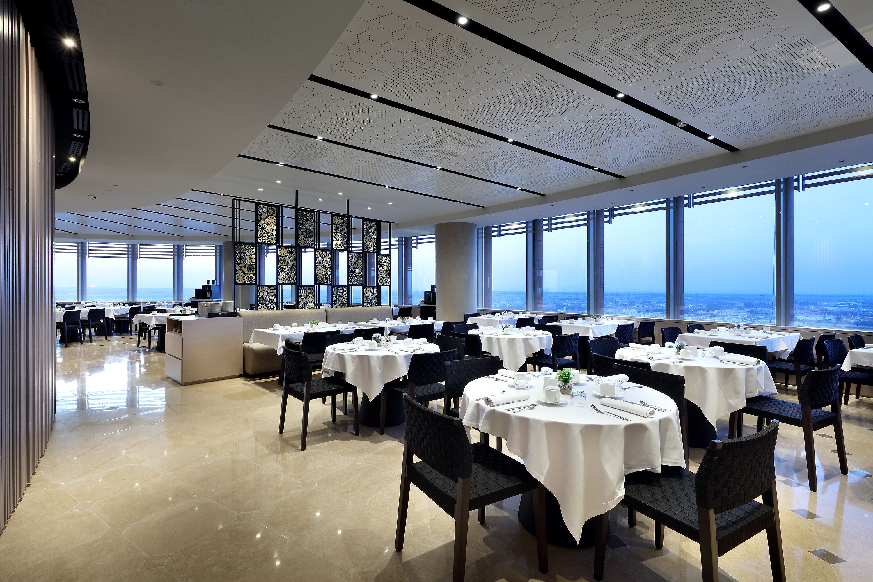 A spacious dining area with round tables, chairs, and a view of the ocean.