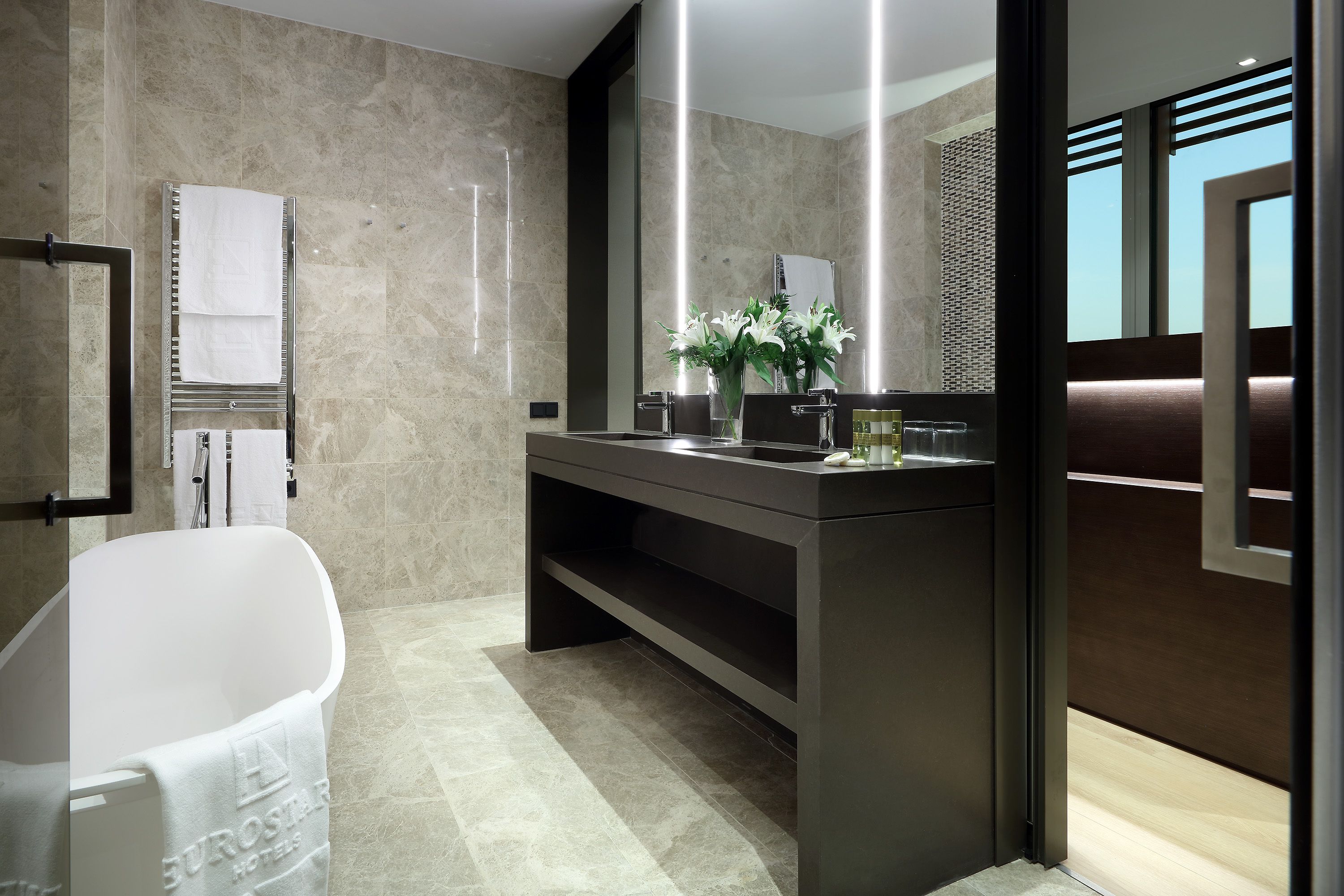 Un baño moderno con bañera, tocador con espejo y un florero con flores.