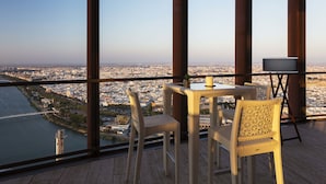 A balcony with wicker chairs and a table, overlooking a cityscape and river. - Eurostars Torre Sevilla (Seville)