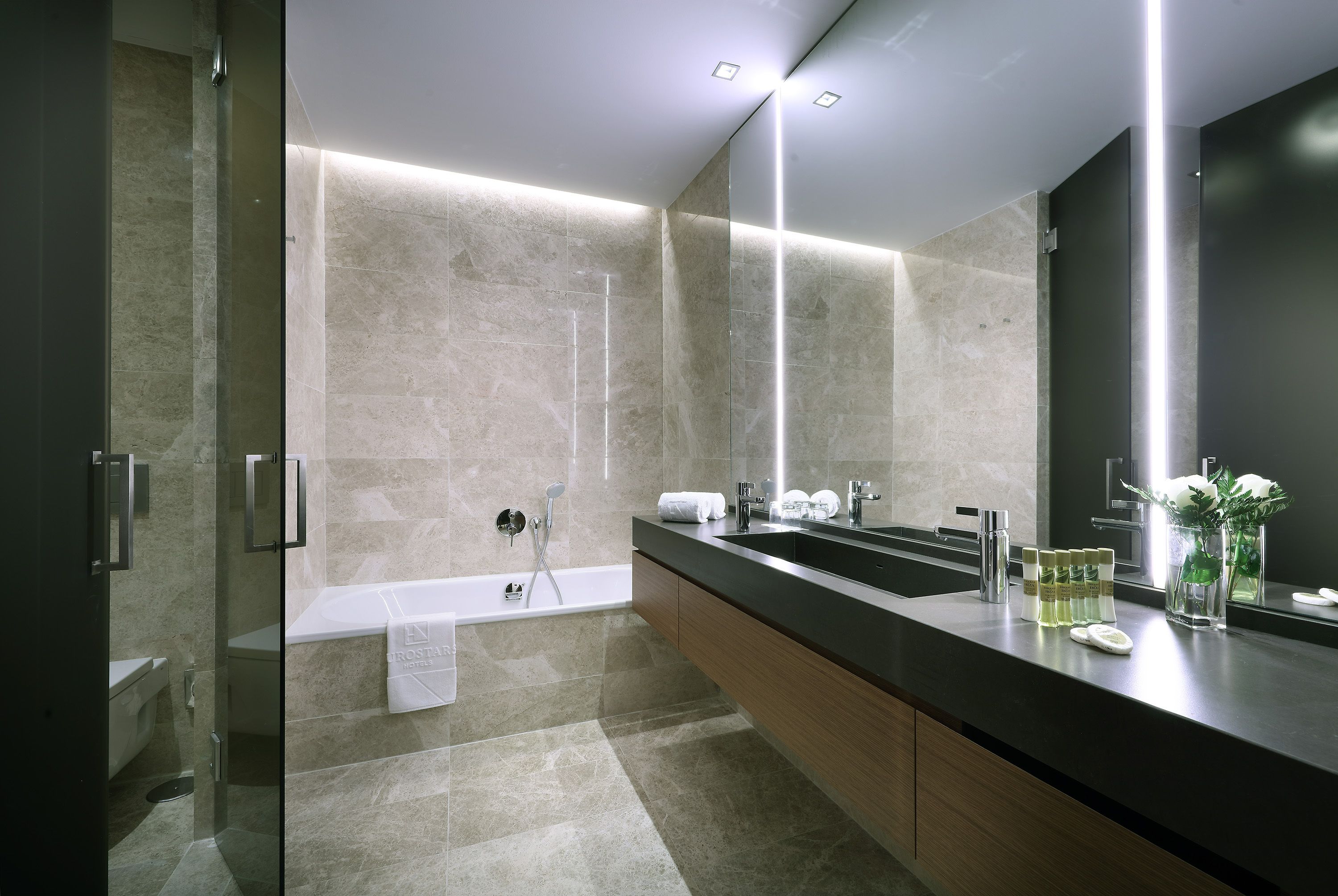 Un baño moderno con ducha envuelta en vidrio, un espejo grande y un tocador con encimera negra.